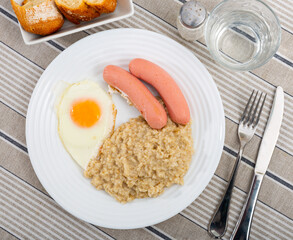 Breakfast is made from boiled oatmeal, fried egg and boiled sausages.