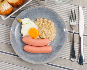 Continental breakfast for one person - portion of oatmeal, fried egg and sausage. Food close-up, eggs with sausage and porridge