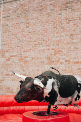 Bull riding attraction at a local fair with a mechanical cow on a red inflatable surface
