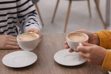 Coffee break. Women with cups of hot drinks at wooden table indoors, closeup