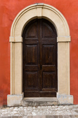 Historic wooden doorway with stone arch frame in vibrant red wall.
