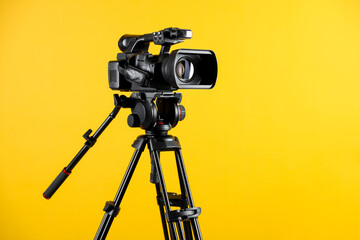 Modern video camera with tripod on yellow background, space for text