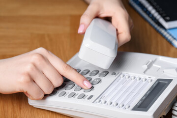Woman dialing number on telephone at wooden table, closeup