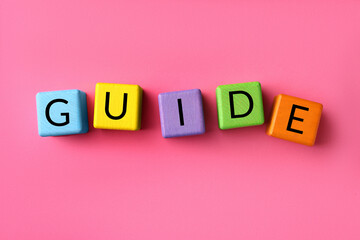 Word Guide made of colorful cubes on pink background, flat lay