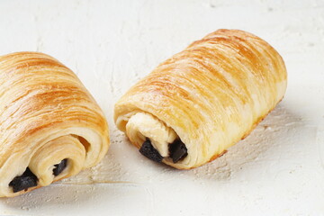 A single pain au chocolate pastry placed on a white textured surface, showcasing its golden, flaky layers and rich chocolate filling.