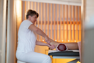 Foot Massage Therapy in a Relaxing Spa Setting. A professional massage therapist in a white uniform...