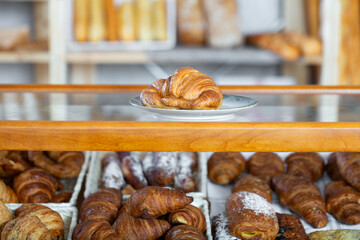 Fresh croissant with a golden crust on a plate in the bakery. Fragrant pastries for breakfast