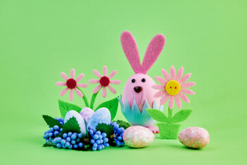 funny toy easter pink bunny preparing for the holiday with colorful eggs and flowers on a green background