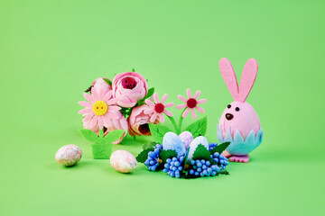 nice toy pink bunny getting ready for the easter holiday with colorful eggs and flowers on a green background