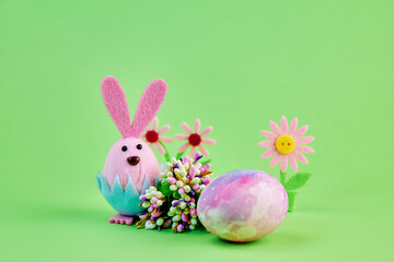 funny toy pink bunny celebrates the holiday of Easter with a large colorful egg and flowers on a green background