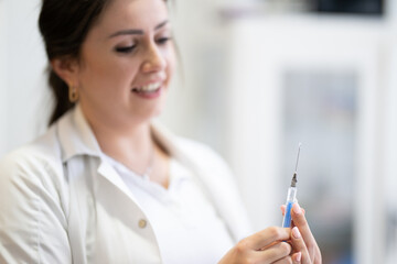 A focused nurse in a white lab coat carefully prepares a syringe for an injection in a professional healthcare environment. © .shock