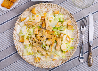 Portion of diet Caesar salad is served for lunch. Dish is prepared from chicken pieces, romaine lettuce leaves, wheat croutons and garnished with quail eggs.