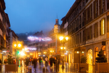 Scenic night view of illuminated busy Chambery pedestrian street of Place Saint-Leger during winter Christmas season with bright lighting and traditional decorations, France.
