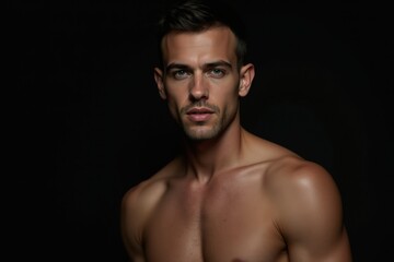 Fototapeta premium Handsome shirtless male model with chiseled features and toned physique posing against a dark background, highlighting masculine beauty, confidence, and fitness aesthetics