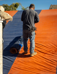 A man working on draping an orange and blue fumigation tent on a house