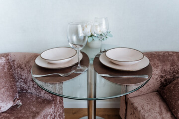 A modern glass table adorned with an elegant arrangement of plates, utensils, and sparkling wine...