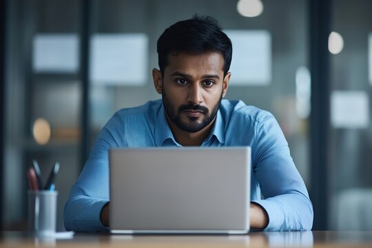 Indian businessman staring at laptop screen deeply focused on his work seated in workplace, analyze received document, review data, consider decision, working on financial report and business strategy