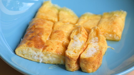 roll omelette stuffed with chesse and rice on blue plate, delicious food in the morning