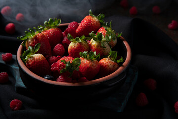 Close up of a black ceramic tray filled with red berries, strawberries, raspberries, and blueberries on a black table with raspberries