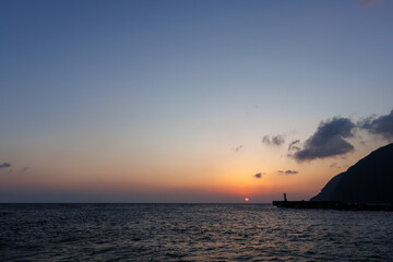 Fototapeta premium 三原山と灯台のシルエット。 夜明けの底土港と底土海水浴場の日の出。 東京都伊豆諸島八丈島-2025年 