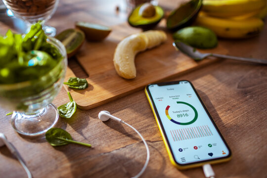 Healthy smoothie ingredients and fitness tracking app on smartphone with banana avocado and spinach on kitchen table