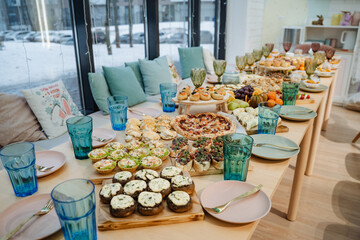 A long and beautifully arranged table set with plates, glasses, and delicious cupcakes placed elegantly on it for a gathering or a special event. It creates a warm and inviting atmosphere