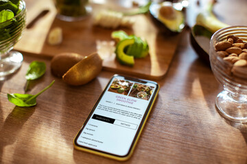 Smartphone on kitchen counter with green smoothie recipe on screen surrounded by healthy ingredients