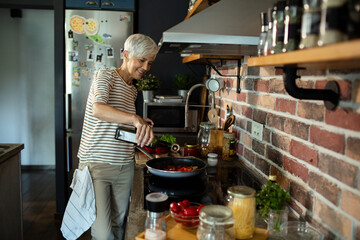 Senior woman cooking in modern home kitchen pouring oil into pan healthy meal preparation