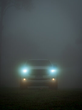 Chaiyaphum, Thailand - August 09, 2024: White Ford Ranger pickup truck, vehicle emerges from thick fog, its headlights shining brightly, in an open field, in natural environment.