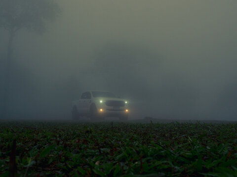 Chaiyaphum, Thailand - August 09, 2024: White Ford Ranger pickup truck, vehicle emerges from thick fog, its headlights shining brightly, in an open field, in natural environment.