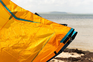 Close up detail of one bright orange kite surfer, wing kite equipment lies on sand on bright sunny day. Active sports travel concept