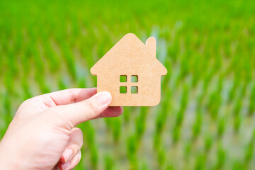 Conservationists hold up a house symbol against a background of growing rice, the concept of sustainable coexistence with nature and a self-sufficient economy.