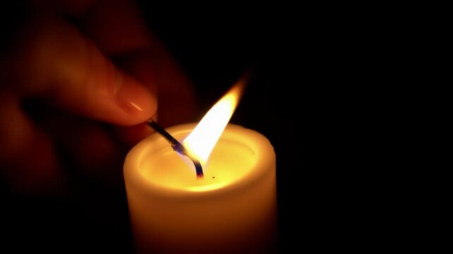 Illumination and transition: A hand carefully lights a second candle from the flame of the first, then gently extinguishes the original, capturing the delicate interplay of light, shadow, and the ephe