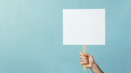 Hand holding a white blank sign on a light blue background, a concept of political protest or picket