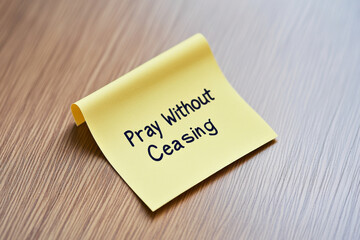 A yellow sticky note with the message "Pray Without Ceasing" rests on a light wood surface.