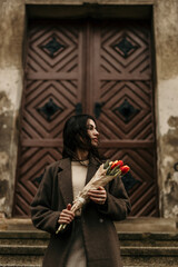 Obraz premium Stylish young woman holding tulips bouquet in front of a church