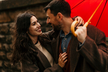 Mid aged couple walking under red umbrella on rainy autumn day
