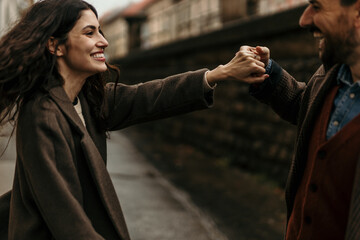 Young woman holding hands with husbant, spinning around and smiling in old European city
