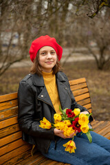 Portrait of a 13-year-old teenage girl in a red beret with a bouquet of tulips in a spring park