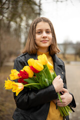 Portrait of a 13-year-old teenage girl in a red beret with a bouquet of tulips in a spring park