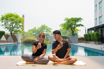young couple doing yoga next to pool and using phone