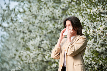 Woman allergic suffering from seasonal allergy at spring in blossoming garden at springtime. Young...