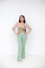 Obraz premium Young Asian woman in floral bustier and pastel green pants smiling with hands on waist against white background