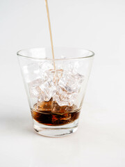 Pouring Cola with Ice in Glass on White Background