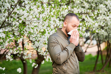 Man allergic suffering from seasonal allergy at spring in blossoming garden at springtime. Man...