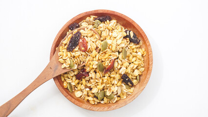 Crunchy granola with oats, nuts, and dried fruits on wooden plate and spoon isolated on white...