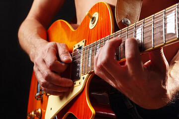Hands of musician playing the orange guitar on dark stage.