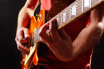 Musician in red plays the orange electric guitar on dark stage.