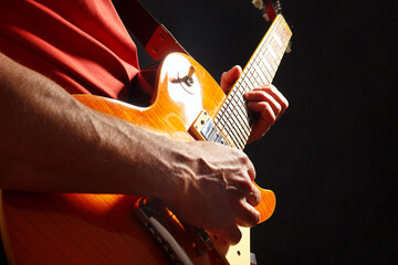 Rock guitarist in red with orange electric guitar on dark stage.