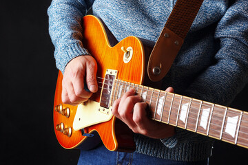 Musician in blue sweater plays the orange electric guitar on dark stage.